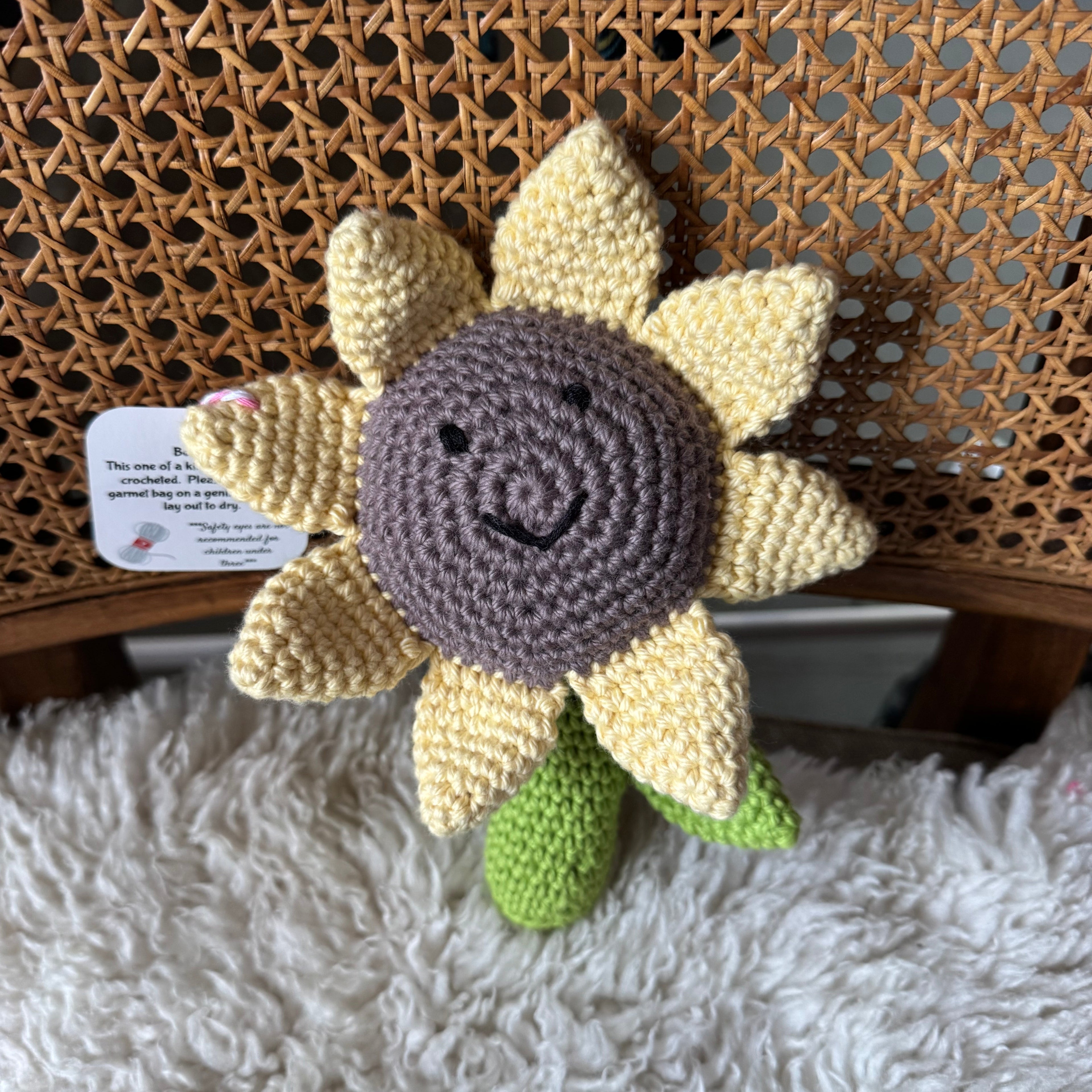 Crocheted sunflower toy with a tag on a textured surface