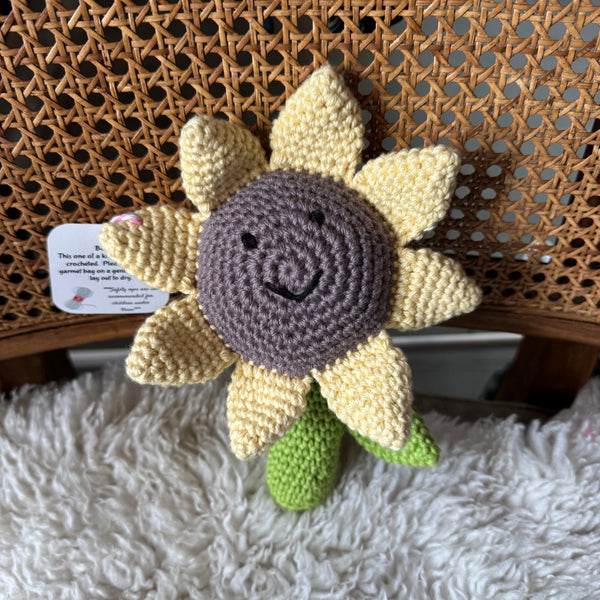 Crocheted sunflower toy with a tag on a textured surface