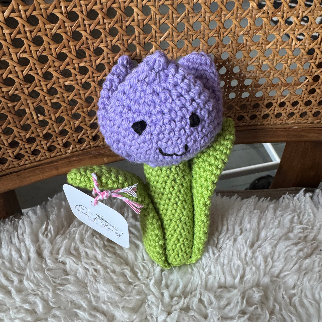 Crocheted purple tulip toy on a textured surface with a fluffy blanket underneath