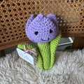 Crocheted purple tulip toy on a textured surface with a fluffy blanket underneath