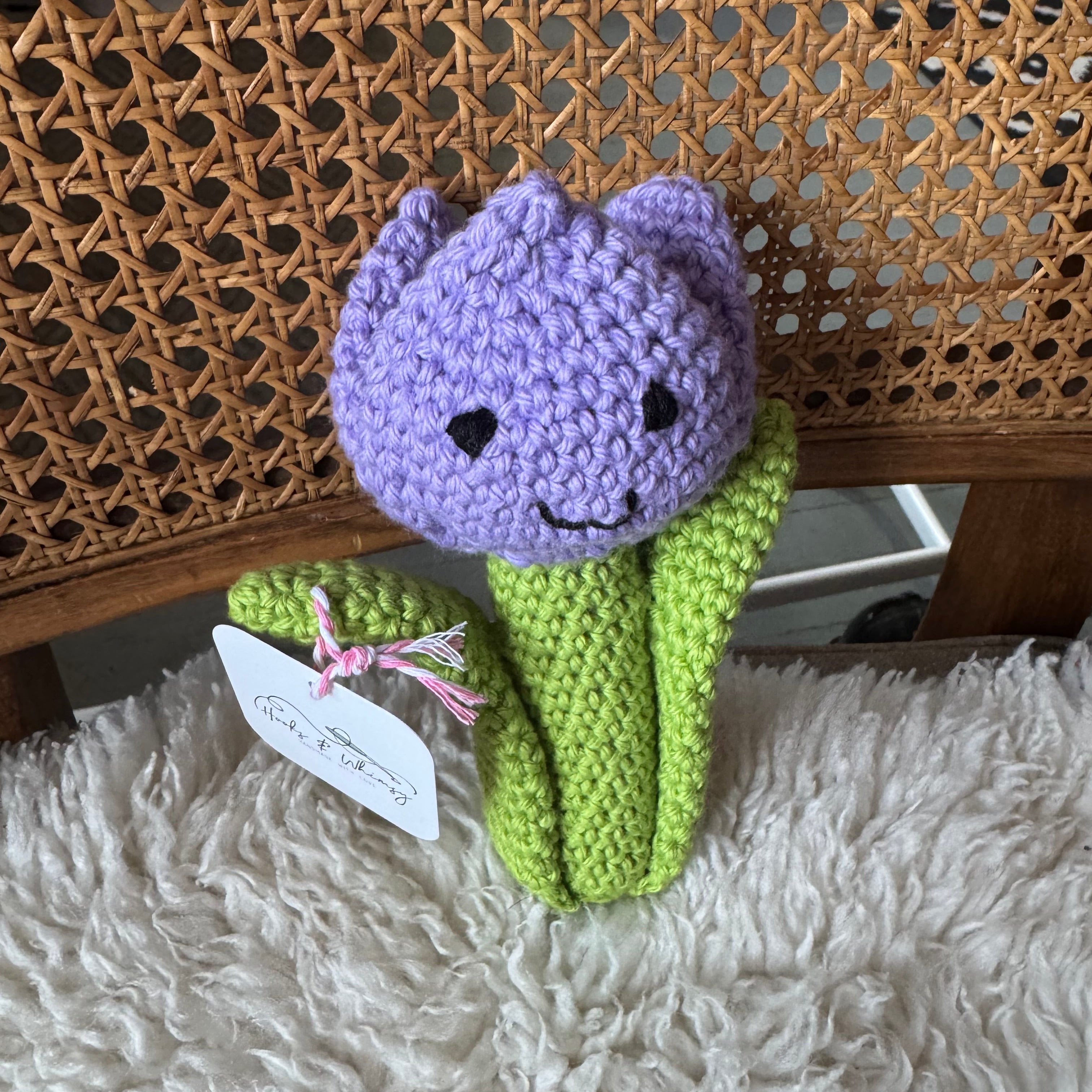 Crocheted purple tulip toy on a textured surface with a fluffy blanket underneath