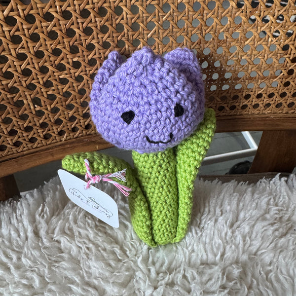 Crocheted purple tulip toy on a textured surface with a fluffy blanket underneath