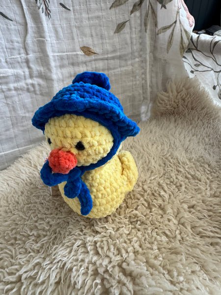 Crocheted toy resembling a duck with a blue hat on a textured surface