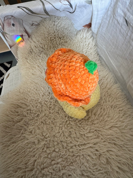 Plush duck toy with a clementine orange hat on a textured surface