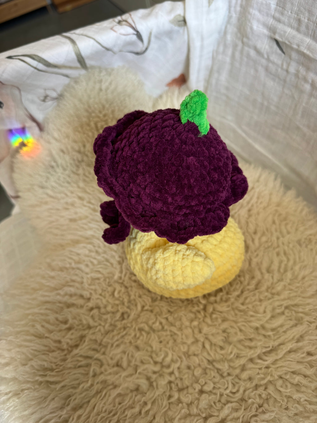 Crocheted purple plum and yellow duck on a textured surface