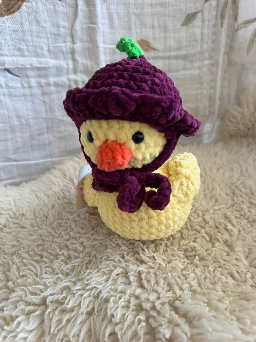 Crocheted duck toy with a purple hat on a textured surface