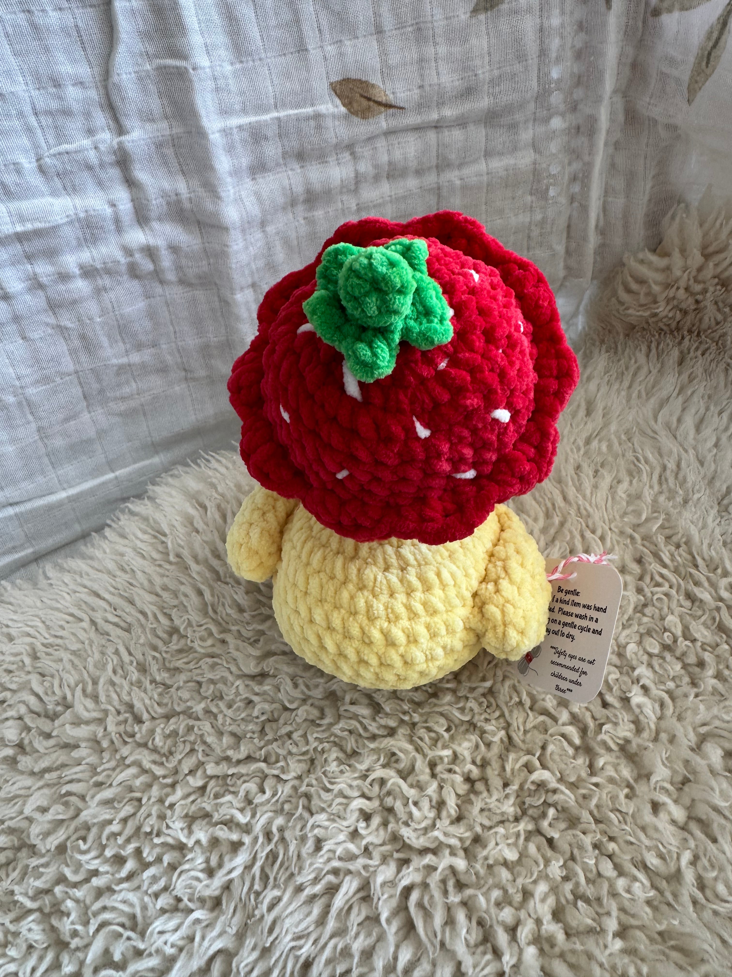 Crocheted strawberry and duck toy on a textured surface