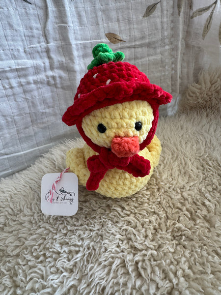 Crocheted toy duck with a red hat on a textured surface
