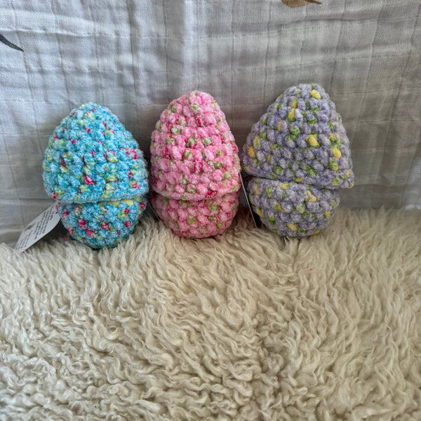 Three crocheted eggs in pastel colors on a textured fabric background