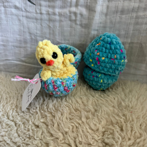 Crocheted toy resembling a bird with a blue head and yellow body on a textured fabric background