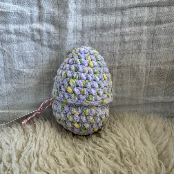 Crocheted egg-shaped toy with a tag on a textured fabric background