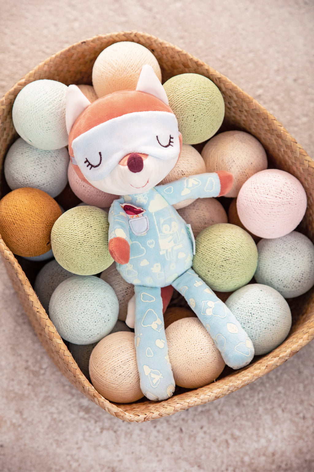 Plush toy fox in pajamas surrounded by colorful balls in a heart-shaped basket