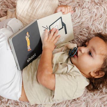 Baby lying on a fluffy surface with a book titled 'shoot' and a basketball illustration.