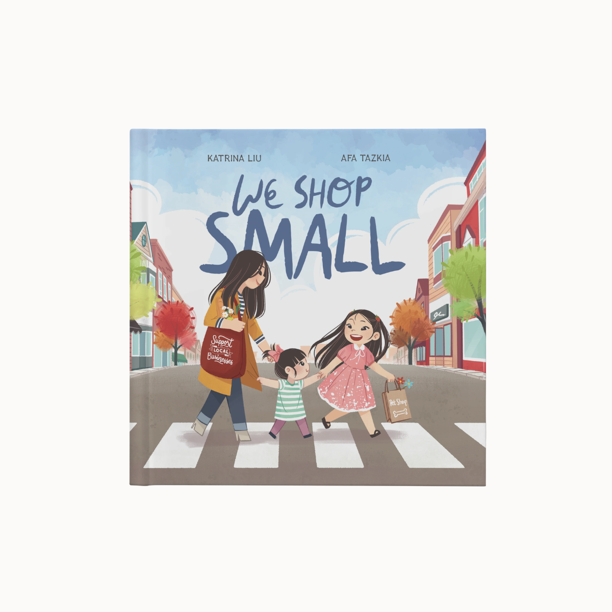 Children's book cover titled "We Shop Small" by Katrina Liu and Afa Tazkia, showing an illustrated mother and child crossing a crosswalk while a daughter joins them, with storefronts and trees in the background.