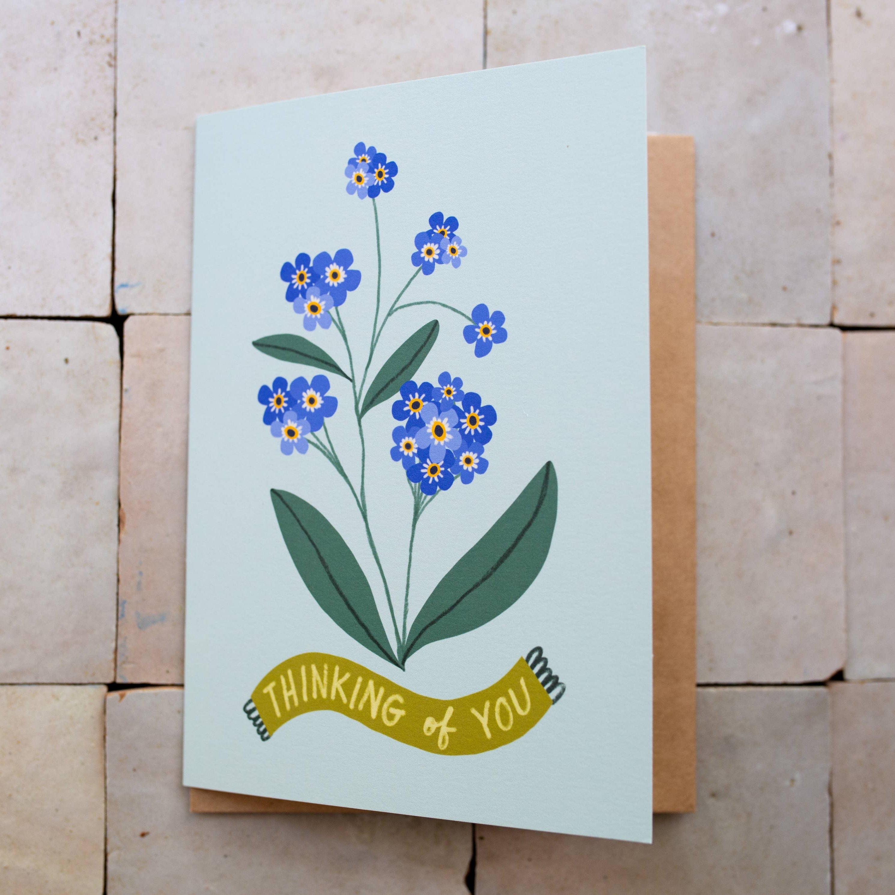 Greeting card with floral design and 'thinking of you' text on a wooden surface