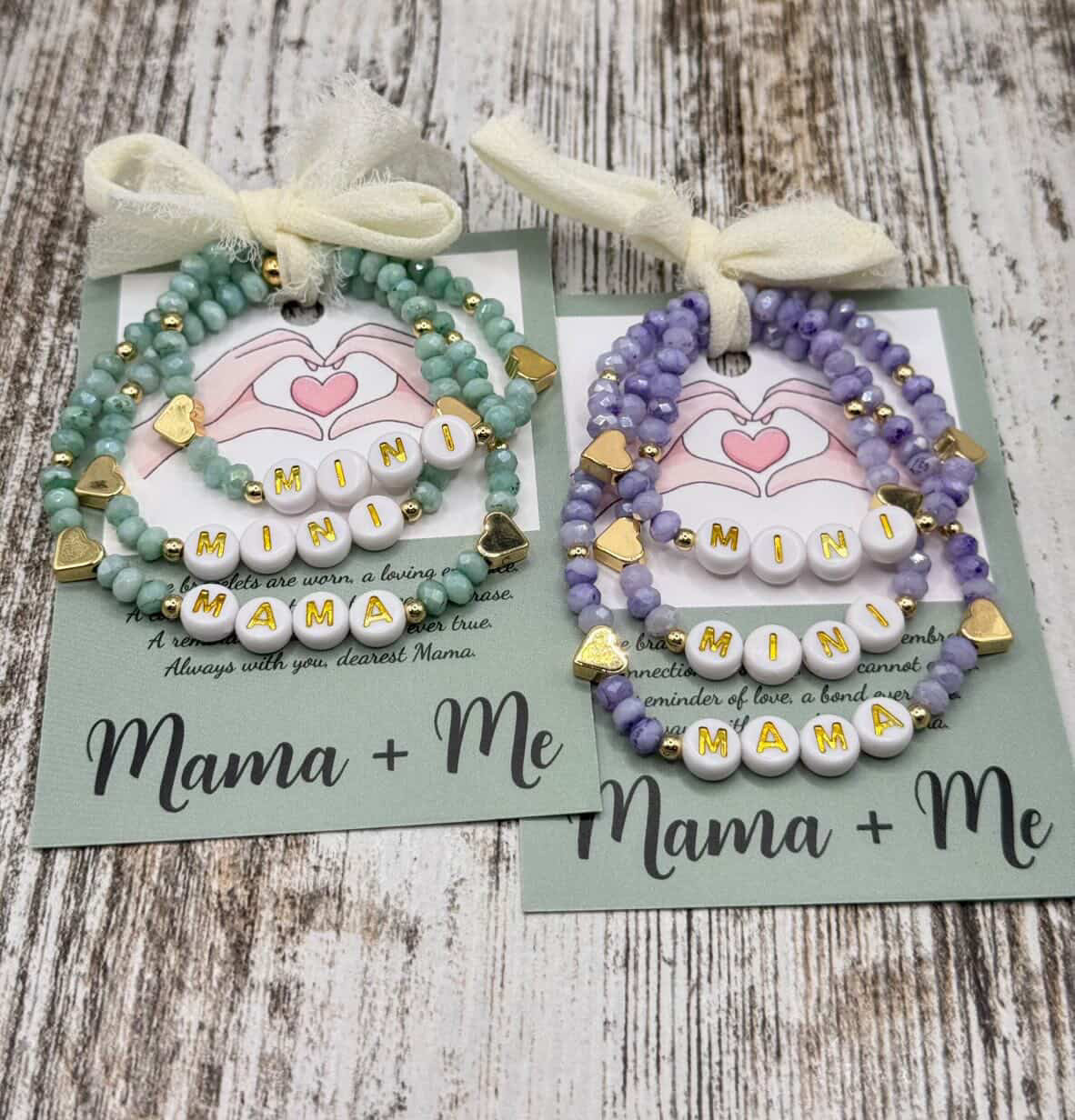 Two 'Mama + Me' bracelets on cards with ribbons on a wooden surface.