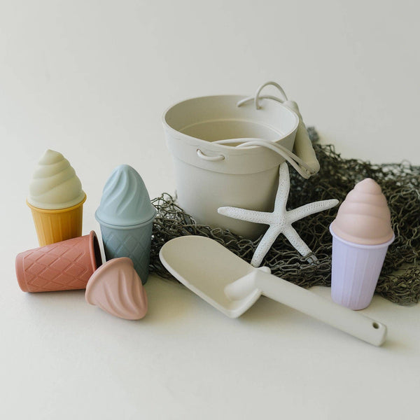 Set of beach-themed toys including a bucket, spade, and molds on a neutral background