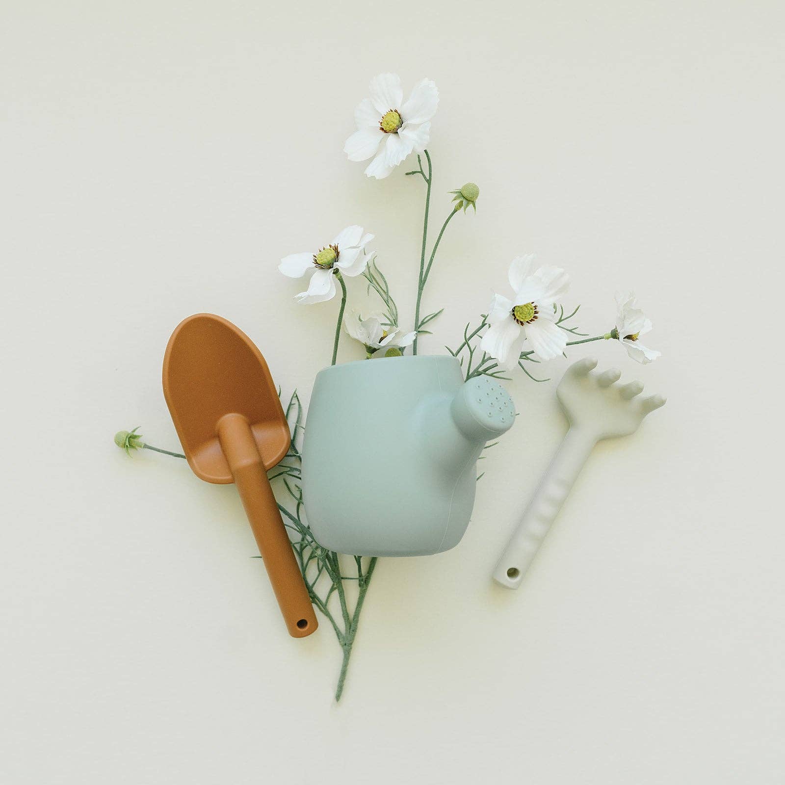 Decorative set with a small green teapot, brown shovel, and white flowers on a light background