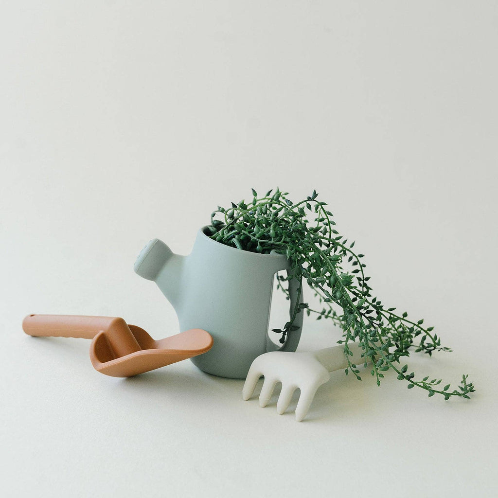 Light blue watering can with a plant and gardening tools on a light background