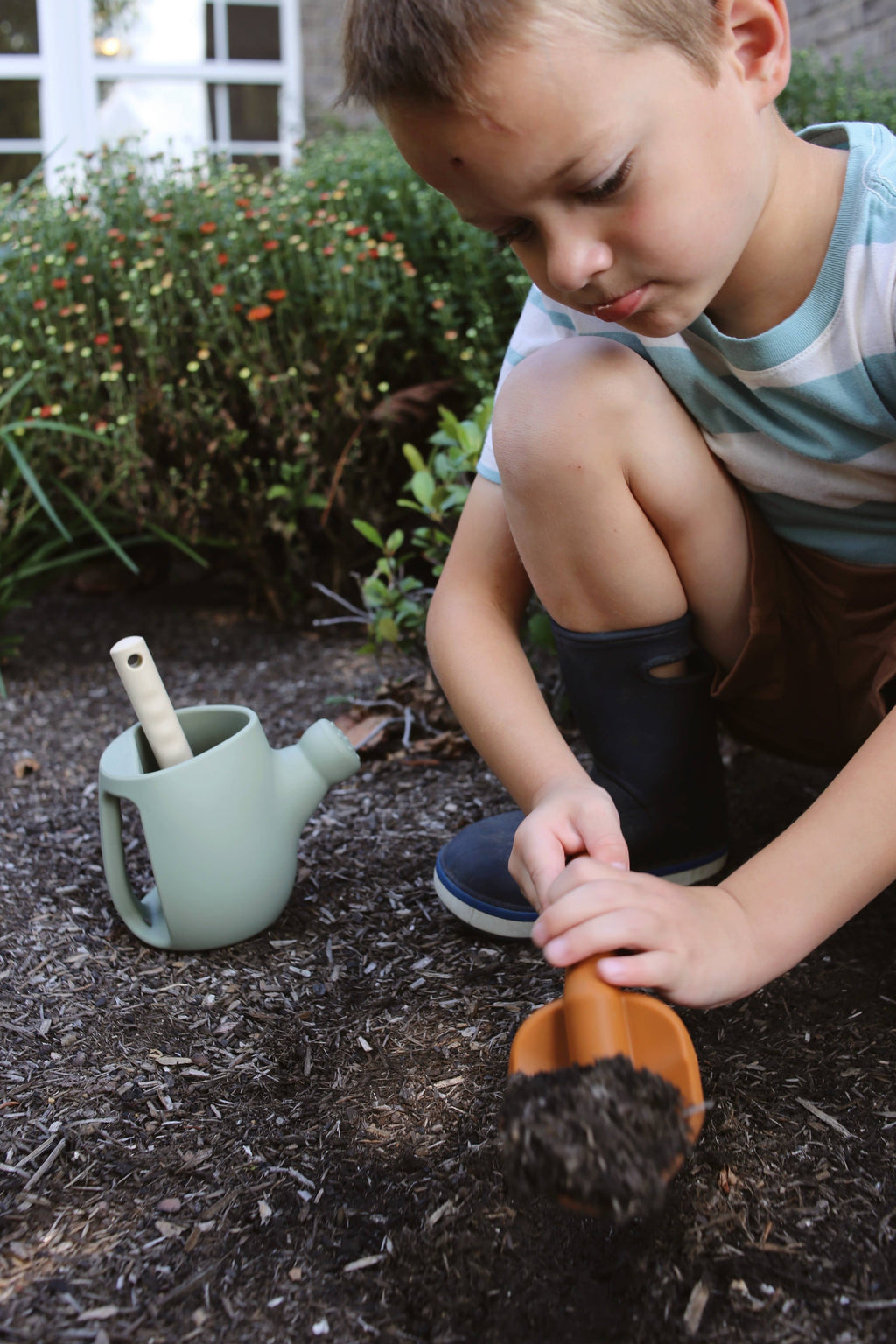 Child playing with a shovel in the dirt, with a watering can nearby.