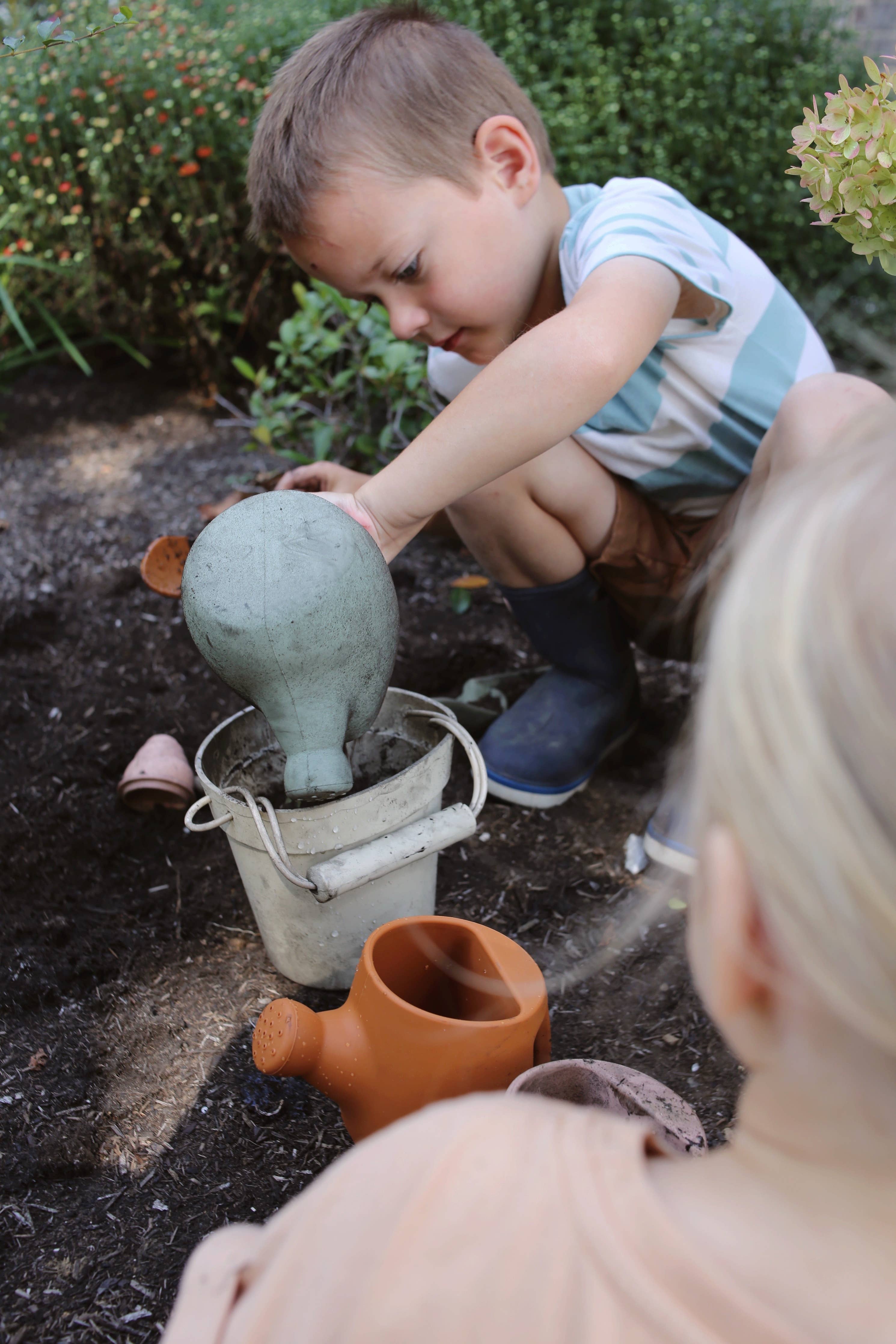 Child playing with a garden gnome and watering can in a garden setting