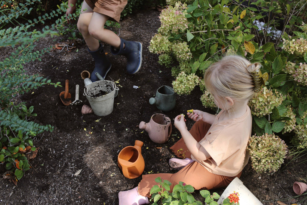 Two children gardening in a garden with pots and tools.
