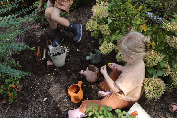 Two children gardening in a garden with pots and tools.
