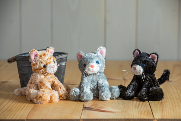 Three stuffed cat toys in different colors on a wooden surface with a white wall background.