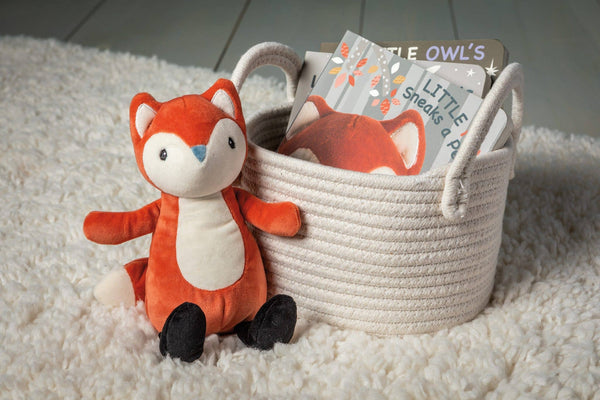Plush fox toy next to a basket with children's books on a soft surface