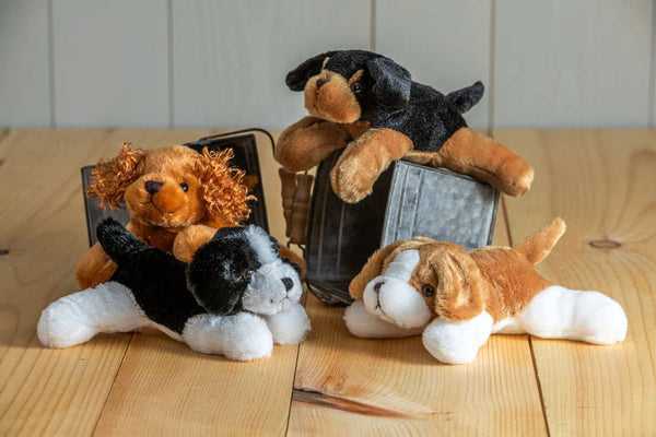 Four plush toys resembling dogs on a wooden surface with a white tiled wall background.