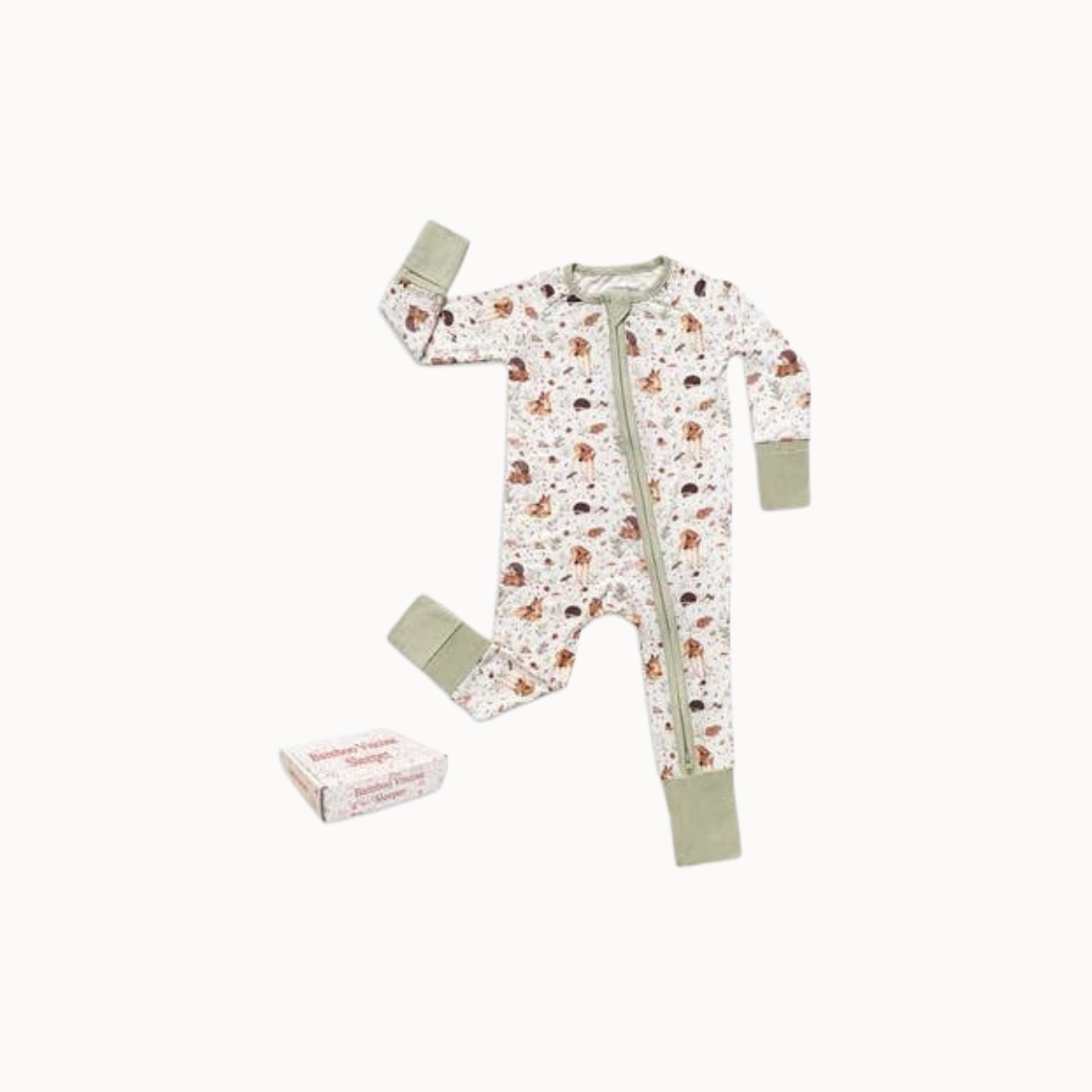 A baby long-sleeve footless one-piece pajama with an allover woodland forest animal print on a white background, featuring sage green cuffs and collar, shown next to its paper packaging box on a light off-white background.