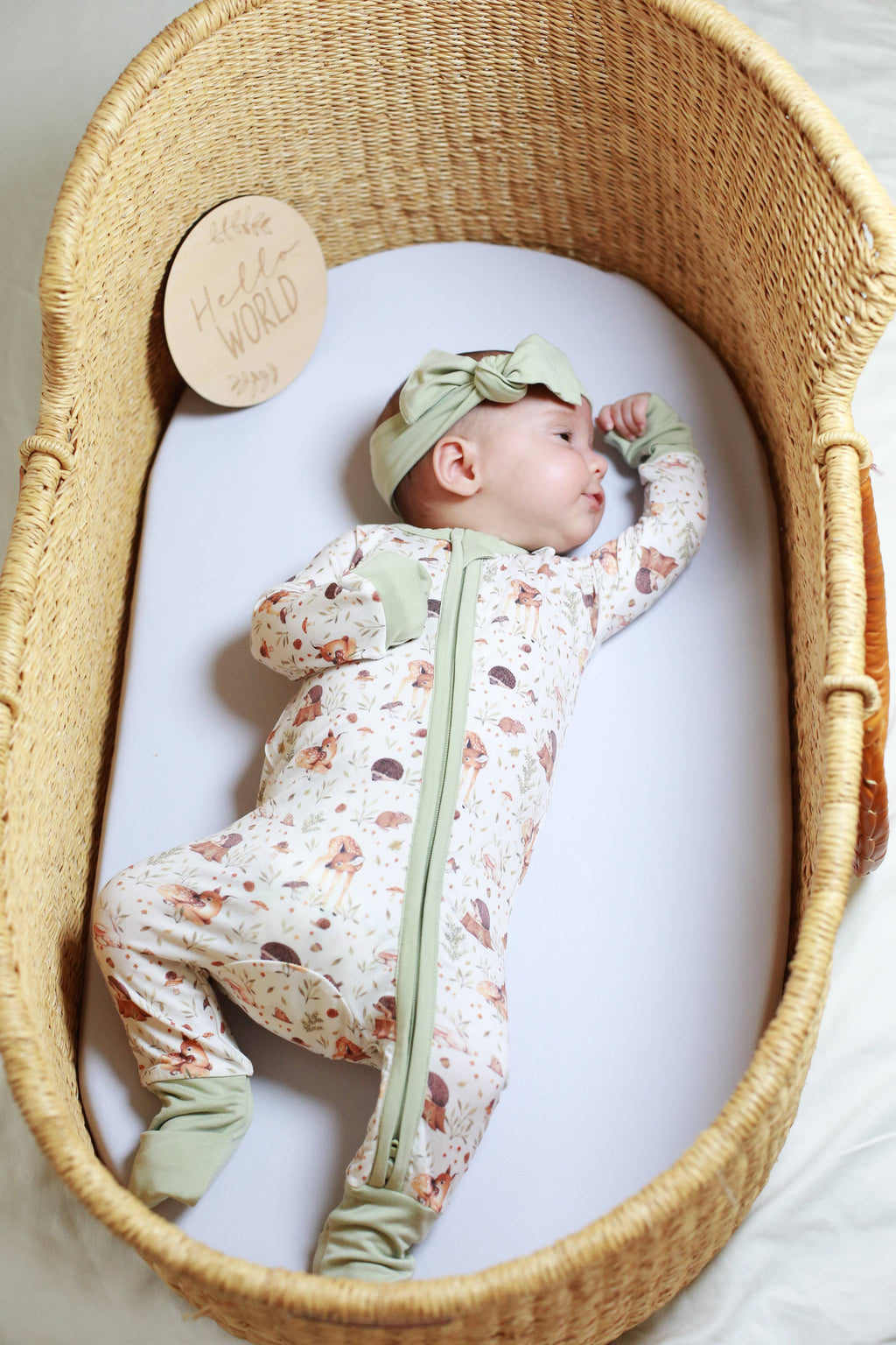 Baby in a floral onesie with green accents lying in a wicker crib.
