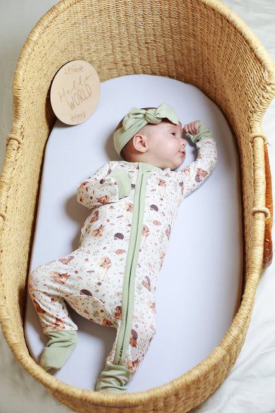 Baby in a floral onesie with green accents lying in a wicker crib.