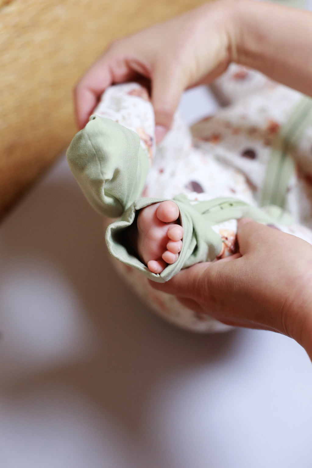 Baby's feet in green socks held by a person's hands with a blurred background