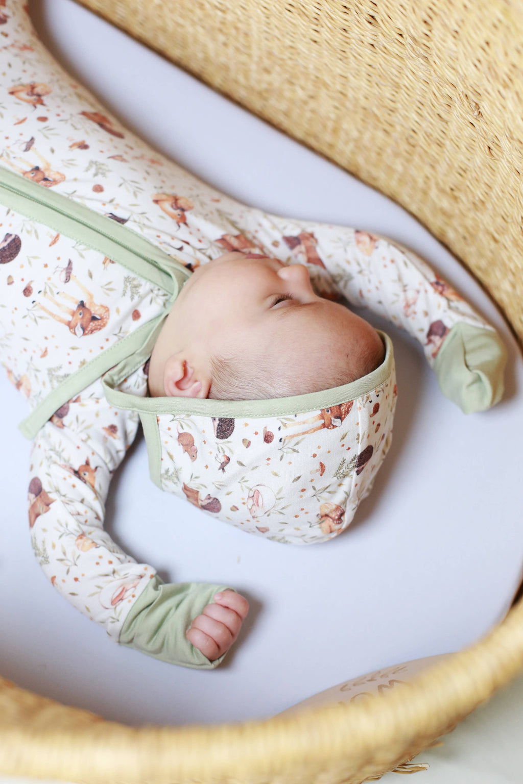 Newborn baby wrapped in a floral blanket with green accents, lying on a white surface.