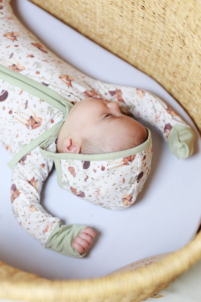 Newborn baby wrapped in a floral blanket with green accents, lying on a white surface.