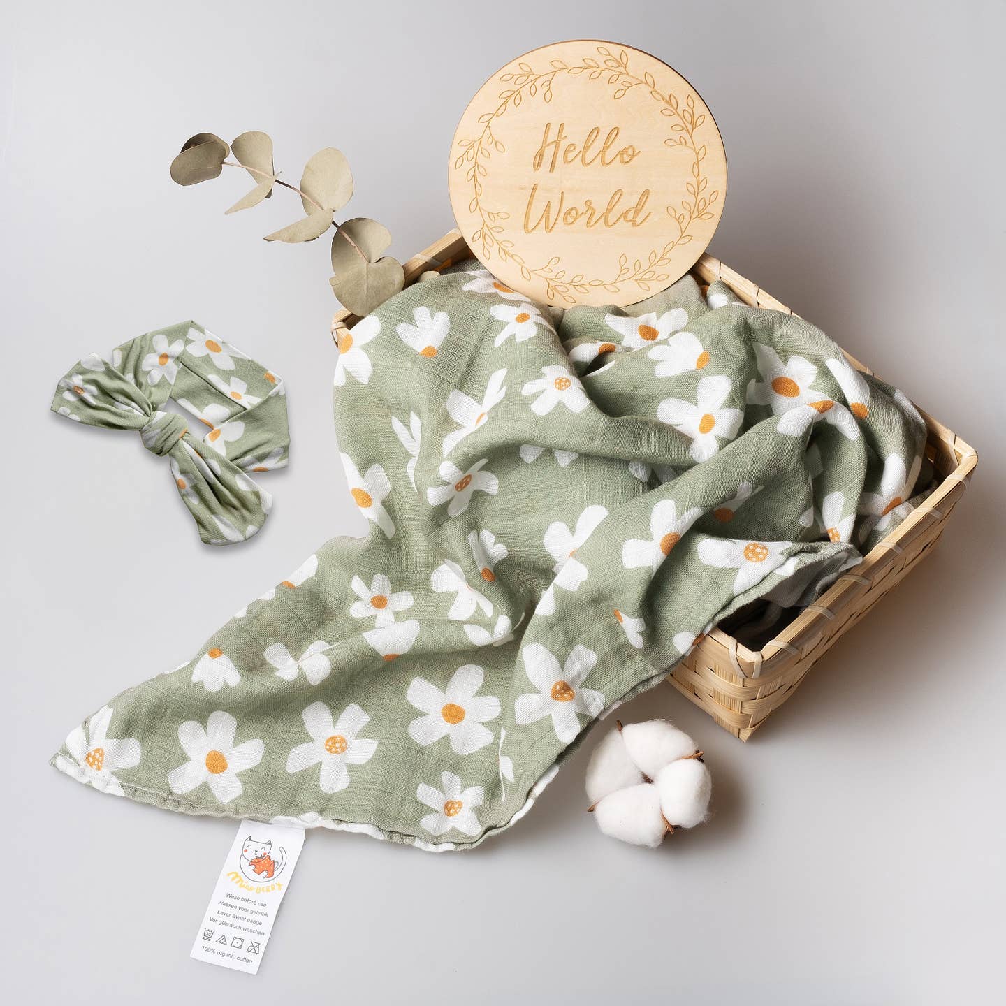 Baby blanket with floral pattern, headband, and 'Hello World' sign on a light gray background