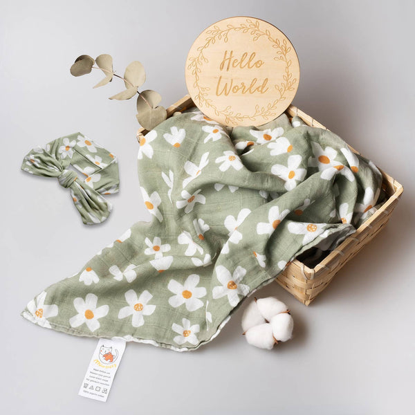 Baby blanket with floral pattern, headband, and 'Hello World' sign on a light gray background