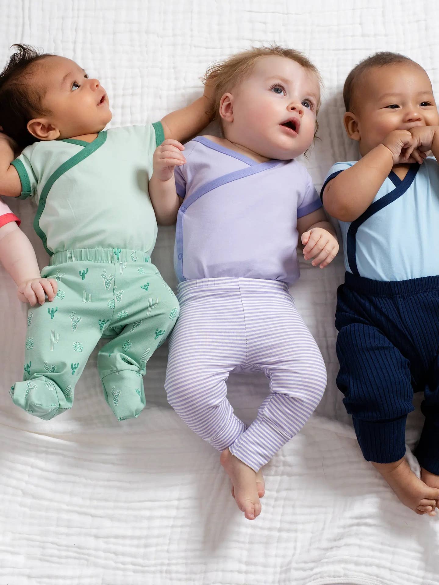 Three babies wearing colorful outfits lying on a white surface