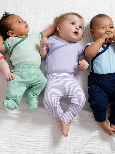 Three babies wearing colorful outfits lying on a white surface