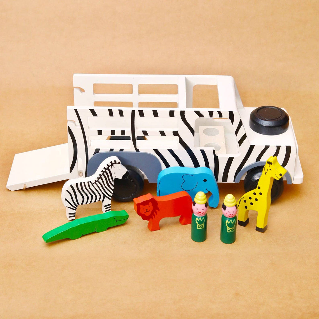 A children's wooden safari-themed toy set on a tan background, featuring a white and black zebra-patterned transport truck with a ramp, plus small animal figures and people figures in green, red, blue, yellow, and orange.