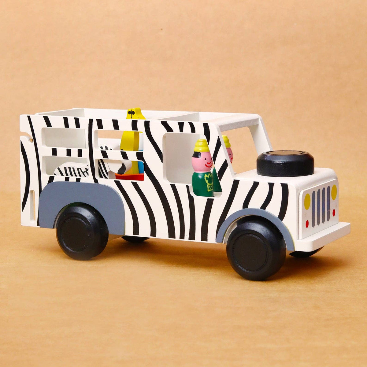 A wooden toy bus with a black and white zebra print, gray side panels, and small colorful character figures inside, photographed on a plain tan background.