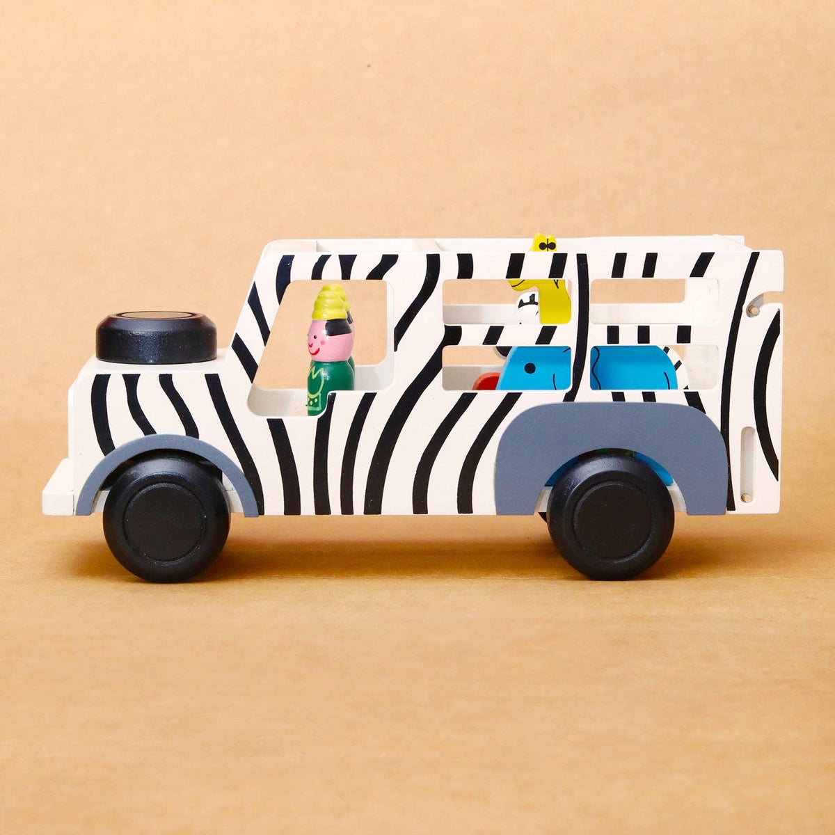 A wooden toy bus with a black and white zebra print, gray wheels and undercarriage, and colorful character figures inside, set against a solid tan background.
