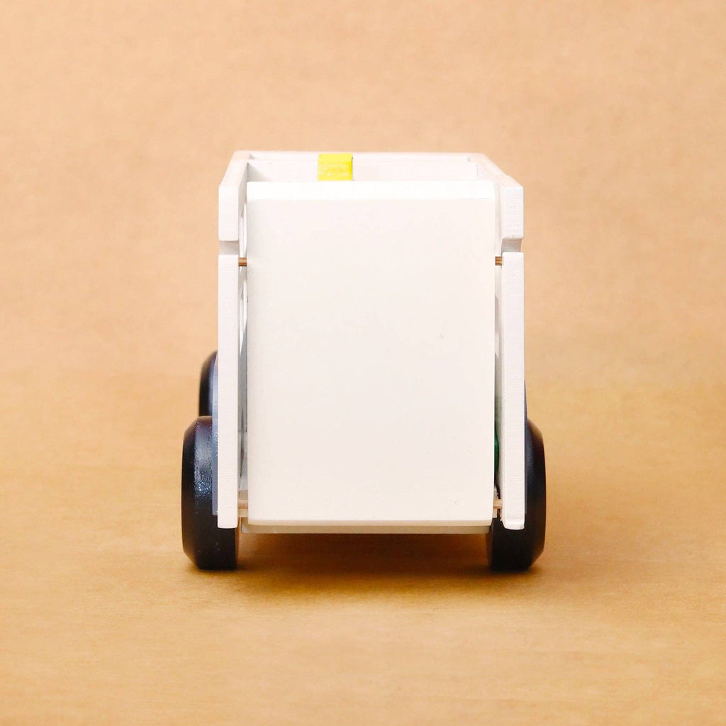 A white plastic toy dump trailer with black wheels, shown from the rear on a plain brown background.