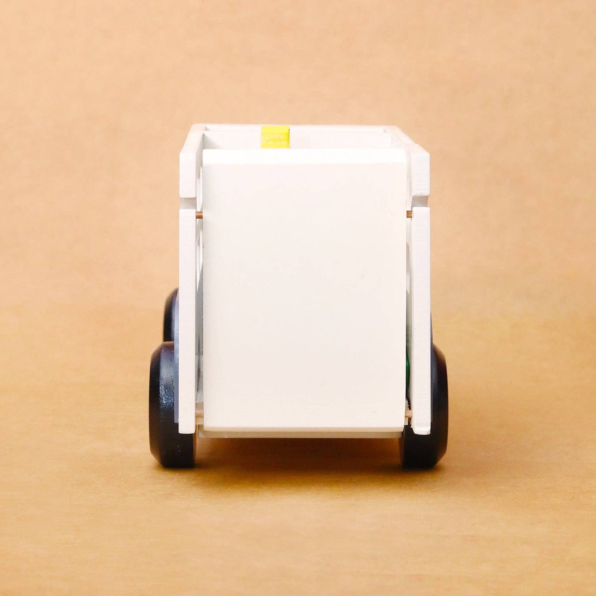 A white plastic toy dump trailer with black wheels, shown from the rear on a plain brown background.