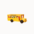 A yellow toy school bus with black wheels and small colorful passenger figures visible through the windows, shown on a plain light gray background.