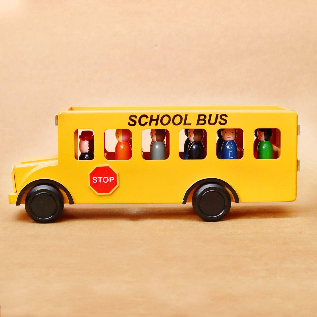 A yellow toy school bus with black wheels and windows, featuring small painted passenger figures inside and a red octagonal stop sign on the side, photographed against a plain tan background.