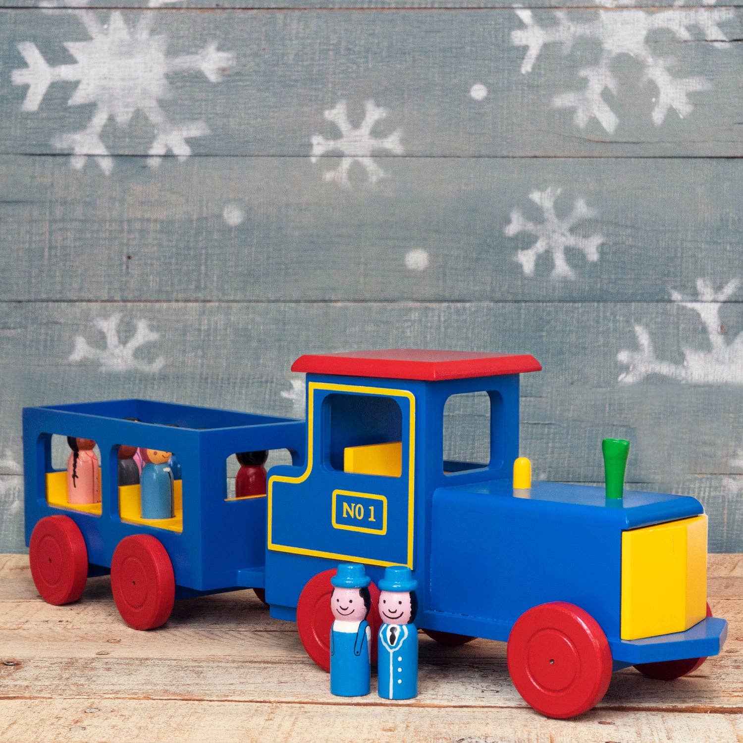 Colorful toy train with two figures on a wooden surface and snowy background