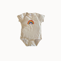 A short-sleeve baby bodysuit in cream-colored cotton, featuring a colorful embroidered rainbow with a white sun and blue sky motif on the chest, displayed against a plain white background.