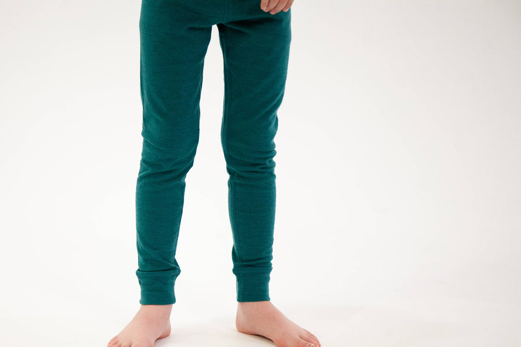 A person wearing dark teal green knit pants, shown from the waist down against a plain white studio background.